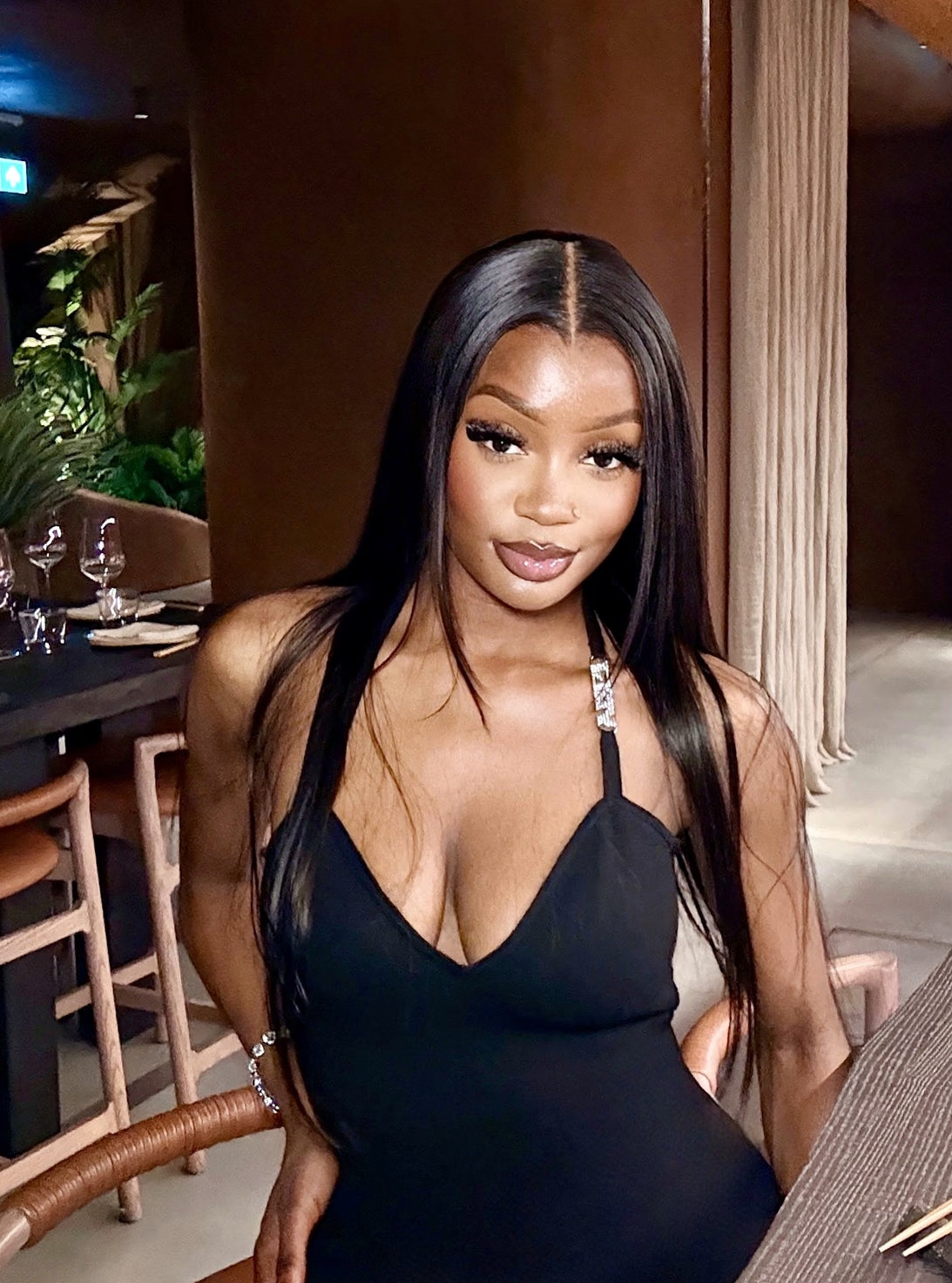 Woman in a black dress sitting at a bar counter in a restaurant.