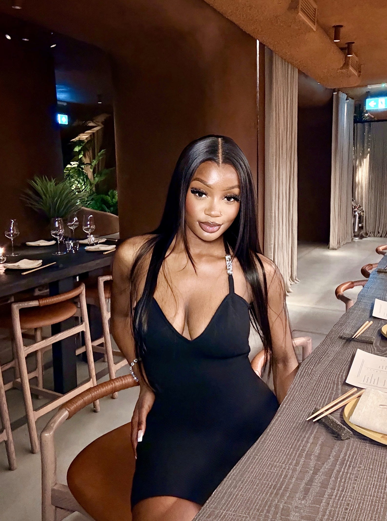 Woman in a black dress sitting at a bar counter in a restaurant.