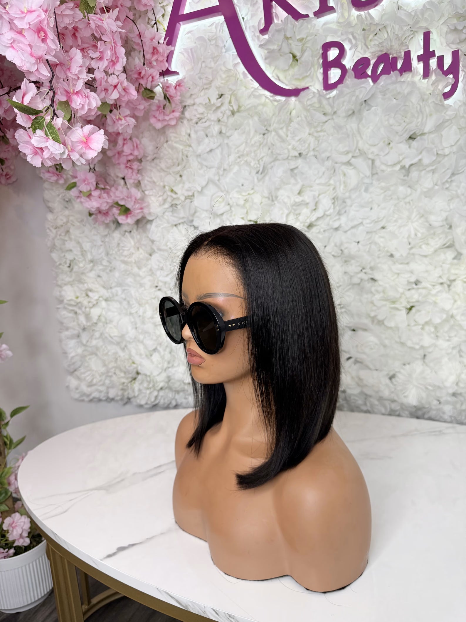 Mannequin head with black wig and sunglasses in front of a floral and &