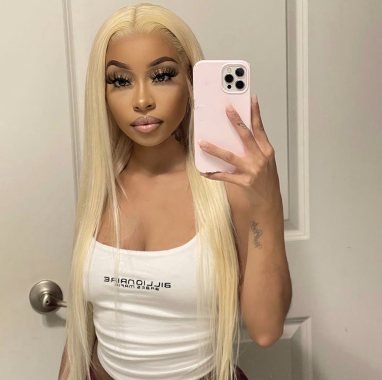 Person with long blonde hair holding a phone in a bathroom setting