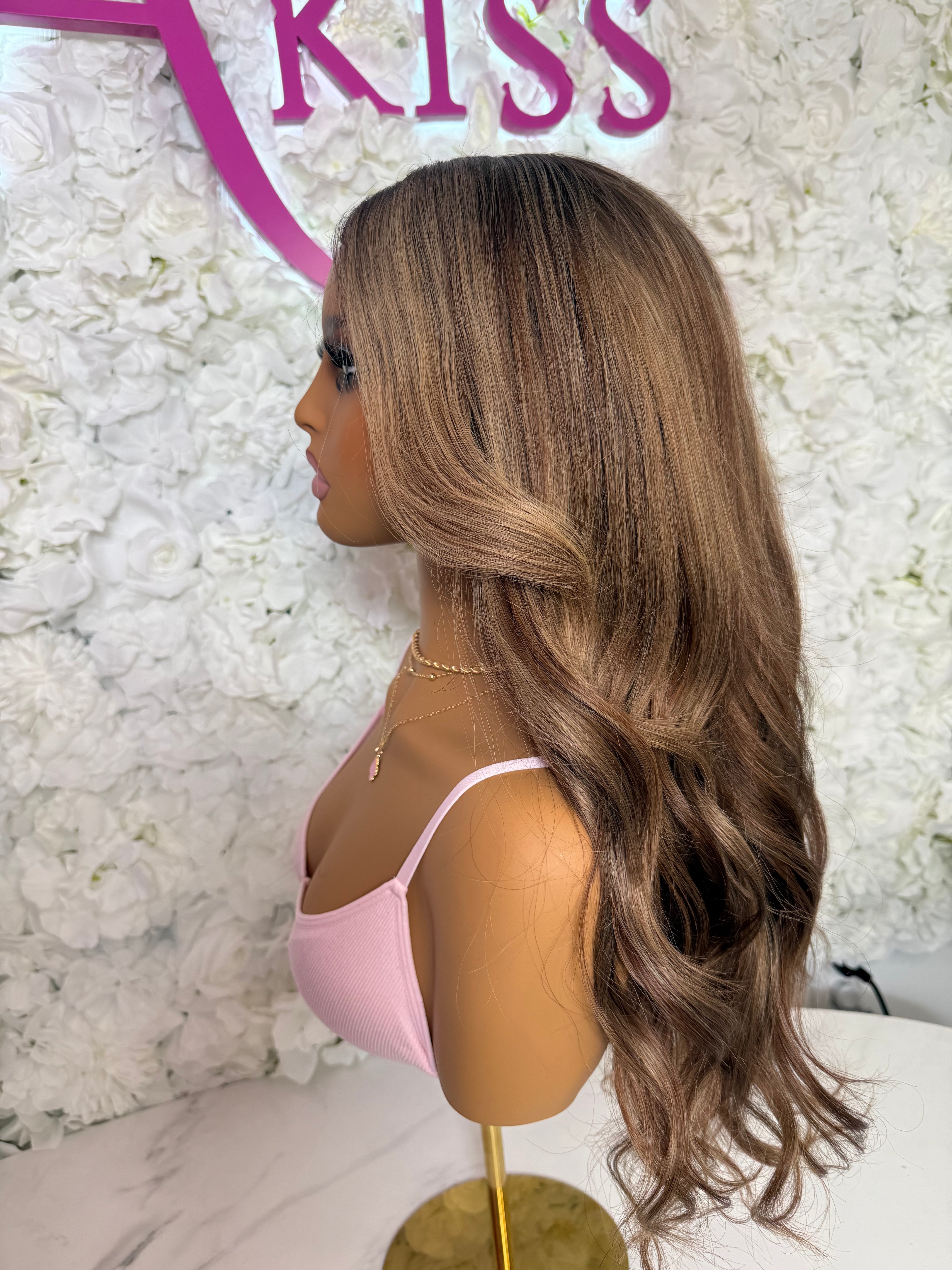 Mannequin head with long brown wig against a floral wall with &