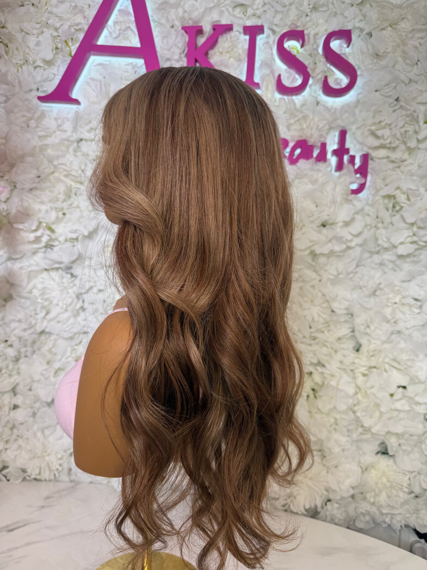 Mannequin head with long brown wig against a floral and &