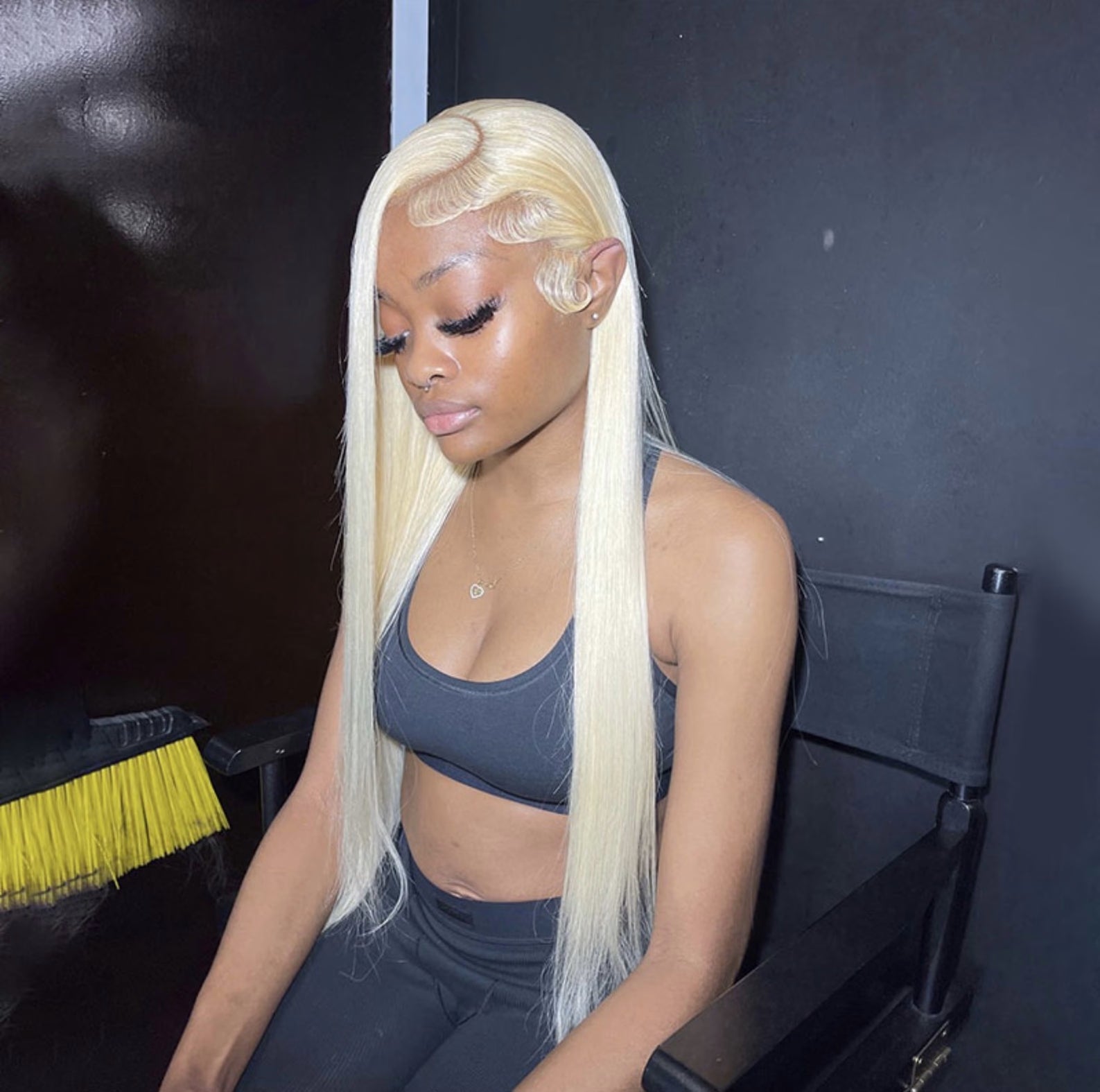 Woman with long blonde wig sitting in a chair against a dark background