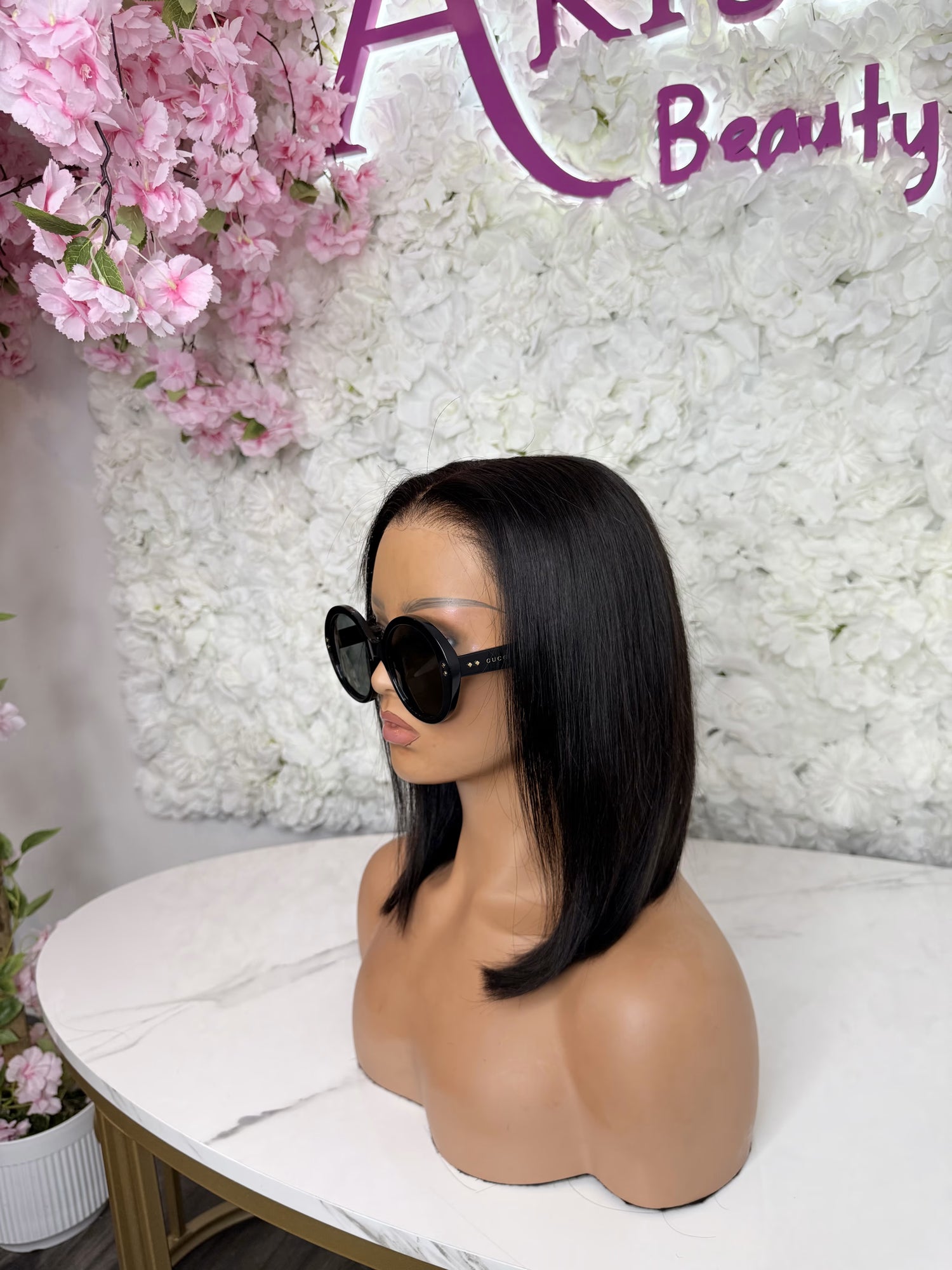 Mannequin head with black wig and sunglasses in front of a floral and &