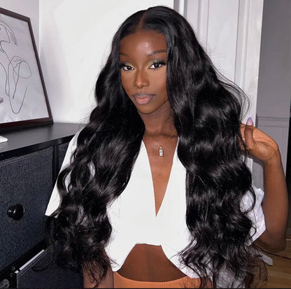 A woman with long, black, wavy hair wearing a white crop top, posing indoors with her hand touching her hair.